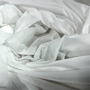 Peut inclure: Tissu blanc transparent avec une texture douce et délicate. Le tissu est drapé et plié, créant un aspect fluide et éthéré.