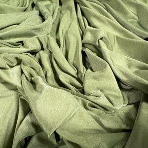 May include: A close-up of a soft, green fabric with a smooth, silky texture. The fabric is draped and folded, creating a variety of folds and creases.