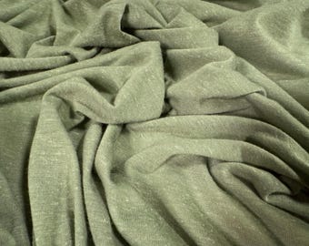 May include: Close-up of olive green fabric with a textured appearance. The fabric is draped and folded, creating shadows and highlights. The material appears to be soft and lightweight, suitable for clothing or home decor.