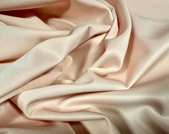 May include: A close-up of a soft, peach-coloured fabric with a smooth, silky texture. The fabric is draped and folded, showcasing its drape and flow.