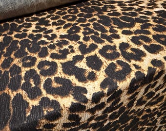 Puede incluir: Primer plano de una tela con estampado de leopardo. La tela presenta grandes manchas negras irregulares sobre un fondo beige, creando un diseño audaz. La tela está doblada, mostrando su textura y caída.