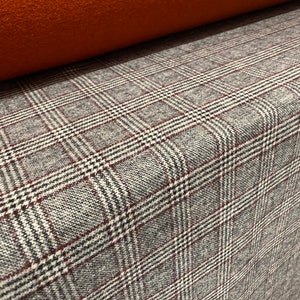 Peut inclure: Gros plan sur un tissu à carreaux gris et blanc avec une fine bande rouge. Le tissu a une apparence texturée et tissée.