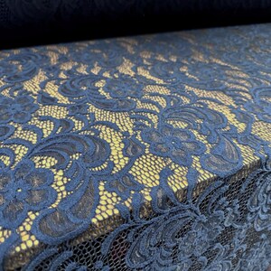 Könnte beinhalten: Nahaufnahme eines marineblauen Spitzenstoffs mit floralem Muster. Die Spitze weist komplizierte Designs und eine zarte Textur auf. Der Stoff ist geschichtet und gibt einen Blick auf eine goldgelbe Rückseite frei.