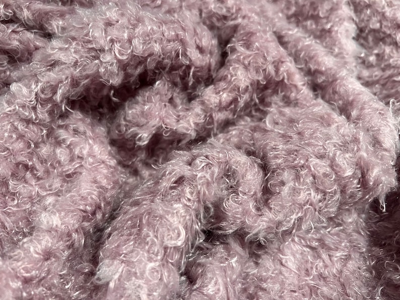 Pu&ograve; includere: Primo piano di un tessuto morbido e soffice di colore malva con una texture riccia.