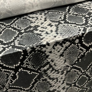 May include: Black and white snakeskin patterned fabric. The fabric has a textured surface and a repeating pattern of black and white scales.