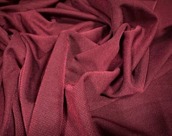 Może przedstawiać: Zbliżenie na głęboki bordowy materiał o fakturowanym, tkanym wzorze. Materiał jest drapowany i złożony, tworząc miękkie, płynne linie.