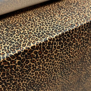 May include: Close-up of a brown and black leopard print fabric. The fabric has a subtle sheen and a soft texture.