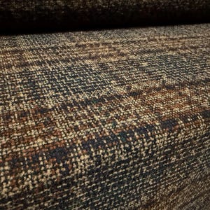 May include: A thick, woven fabric featuring a textured, multi-coloured pattern in shades of dark navy blue, deep brown, and cream. The material displays a dense, interlaced weave with a visible grid-like structure and a rugged, heavy-duty appearance.