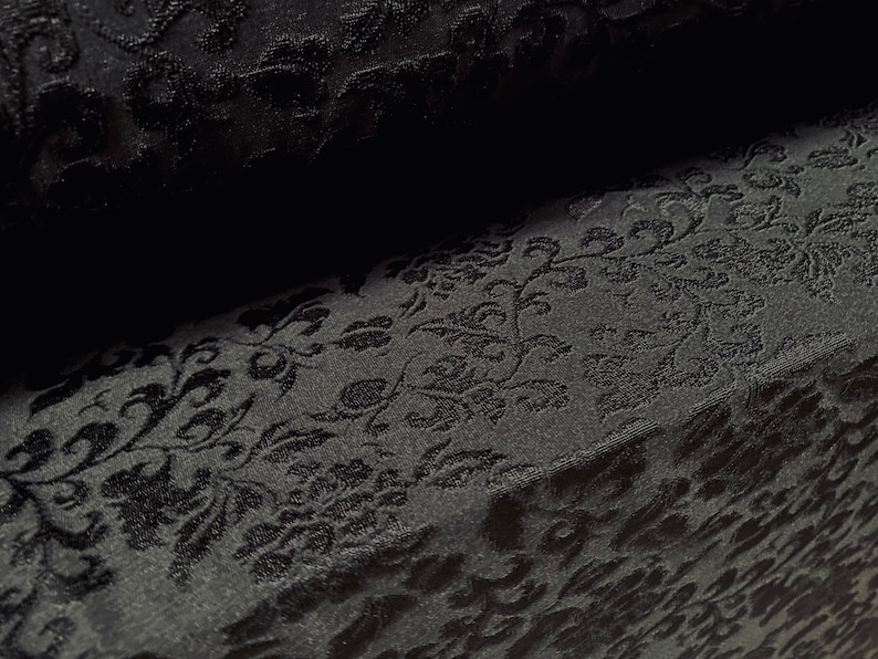 May include: Black fabric with a raised floral pattern. The fabric has a soft, velvety texture.
