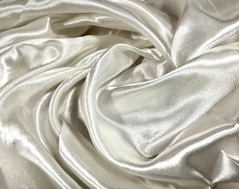 May include: White satin fabric with a smooth, silky texture. The fabric is draped and folded, creating soft, flowing curves.