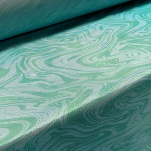 May include: A close-up of a teal fabric with a swirling, marbled pattern in shades of green and white.