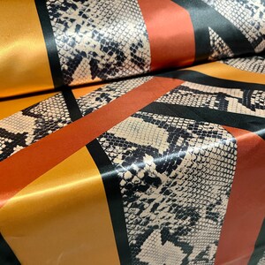 May include: A fabric with a black, white, and brown snake skin pattern. The fabric is cut into strips and sewn together to create a diagonal pattern. The fabric is shiny and has a satin finish.