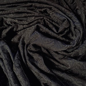 May include: Black fabric with a textured, embossed pattern. The fabric is folded and draped, creating a soft, flowing look.