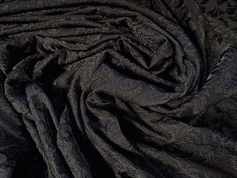 May include: Black fabric with a textured, embossed pattern. The fabric is folded and draped, creating a soft, flowing look.
