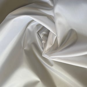Könnte beinhalten: Weißer Satinstoff mit einer glatten, seidenartigen Textur. Der Stoff ist drapiert und gefaltet und erzeugt weiche, fließende Kurven.