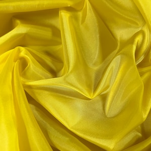 May include: A bright yellow fabric with a smooth, silky texture. The fabric is draped and folded, creating soft, flowing lines.
