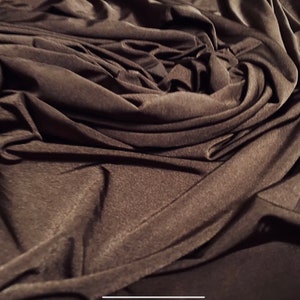 May include: Close-up of a dark brown fabric with a smooth, silky texture. The fabric is draped and folded, creating a soft, flowing look.