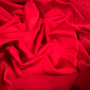 May include: A close-up of a smooth, red fabric with soft folds and wrinkles. The fabric is a deep, rich red color.