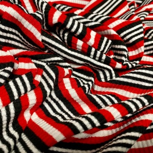 May include: Red and black striped fabric with a ribbed texture. The fabric is folded and draped, creating a dynamic pattern.