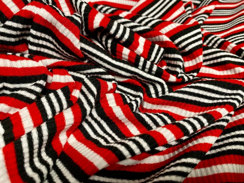 May include: Red and black striped fabric with a ribbed texture. The fabric is folded and draped, creating a dynamic pattern.