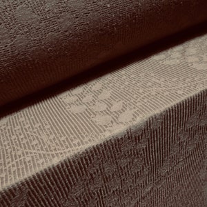 May include: Close-up of a brown textured fabric with a subtle pattern. The fabric is folded in half, revealing a lighter brown fabric with a more intricate pattern.