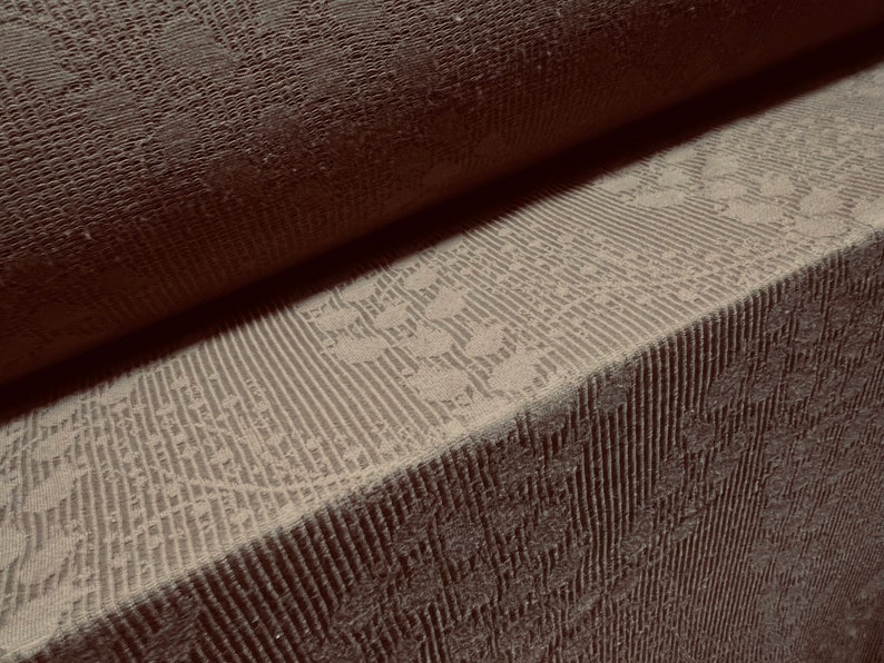 May include: Close-up of a brown textured fabric with a subtle pattern. The fabric is folded in half, revealing a lighter brown fabric with a more intricate pattern.