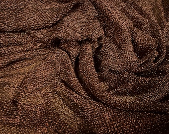May include: Close-up of a brown fabric with a textured, sparkly surface. The fabric is folded and draped, creating a soft, flowing look.