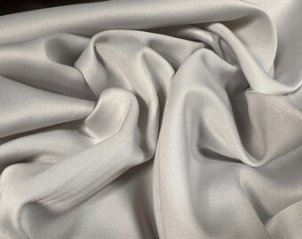 May include: A close-up of a smooth, white fabric with a soft, silky texture. The fabric is draped and folded, creating a luxurious and elegant look.