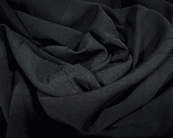 May include: Black fabric with a subtle textured pattern. The fabric is folded and draped, creating soft folds and curves.