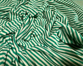 Puede incluir: Tela de rayas verdes y blancas con un tacto suave y texturado. La tela está doblada y drapeada, mostrando el patrón y la textura.