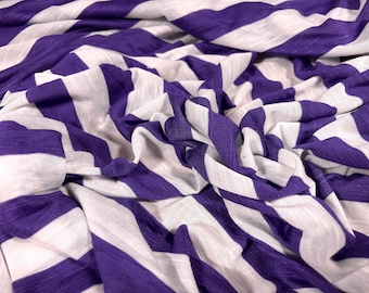 Puede incluir: Tela de rayas moradas y blancas con una textura suave y elástica. La tela está doblada y drapeada, mostrando las rayas en un patrón diagonal.