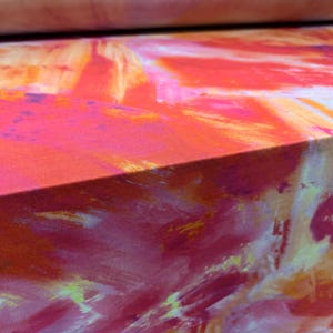 Könnte beinhalten: Abstrakter Stoff mit einem farbenfrohen Design in Orange-, Rosa-, Gelb- und Weißtönen. Der Stoff hat eine strukturierte, pinselstrichähnliche Musterung.