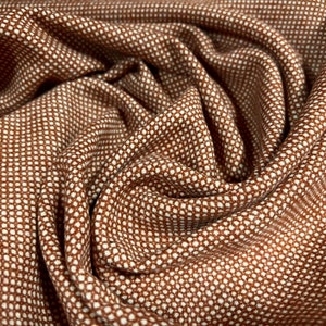 Op de afbeelding: Bruine stof met een wit stippenpatroon. De stof is gevouwen en heeft een textuur.