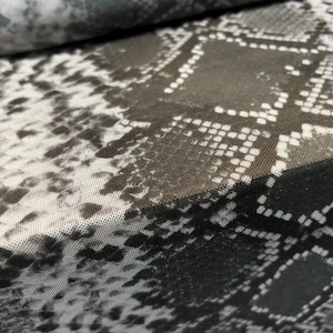 Op de afbeelding: Zwart-witte mesh stof met een slangenhuidpatroon. De stof heeft een subtiele glans en een licht getextureerd oppervlak.