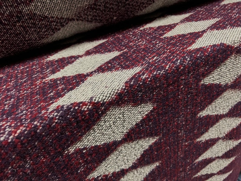May include: Close-up of a burgundy and cream woven fabric with a diamond pattern. The fabric is soft and textured, with a subtle sheen.