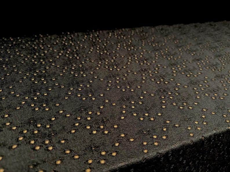 May include: A rectangular black fabric surface featuring a dense, repeating pattern of small, circular gold-colored perforations. The material has a textured, slightly matte finish, and the gold dots are arranged in a scattered, organic layout.