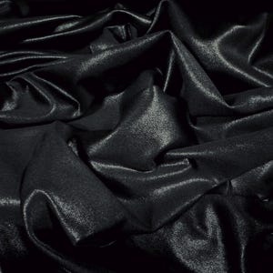 May include: Close-up of a black fabric with a shiny, textured surface. The fabric is draped and folded, creating shadows and highlights. The material appears to be a luxurious textile, possibly satin or silk.