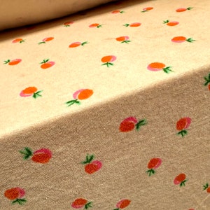 May include: A close-up of a beige fabric with a repeating pattern of pink and orange peaches. The fabric has a slightly textured surface.