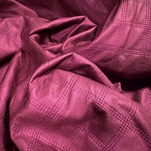 May include: A close-up of a deep burgundy fabric with a quilted diamond pattern. The fabric is soft and textured.