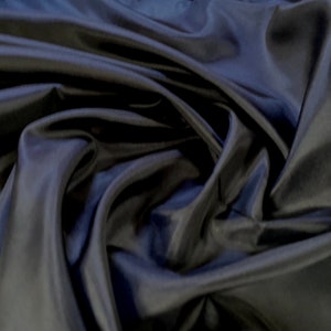 May include: A close-up of a dark blue fabric with a smooth, silky texture. The fabric is draped and folded, creating soft, flowing lines.