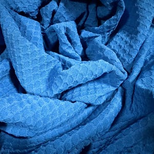 Pode incluir: Um close-up de um tecido azul texturizado. O tecido tem um padrão de waffle e é macio e felpudo.