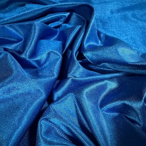 Può includere: Primo piano di un tessuto blu vibrante con una sottile lucentezza. Il materiale è pesantemente drappeggiato, creando pieghe e ombre profonde che evidenziano la trama. Il tessuto sembra essere di peso medio, possibilmente adatto per abbigliamento o scopi decorativi.