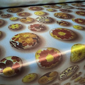 May include: A white fabric with a repeating pattern of yellow, brown, and red floral designs. The floral designs are arranged in a circular pattern, resembling stones.