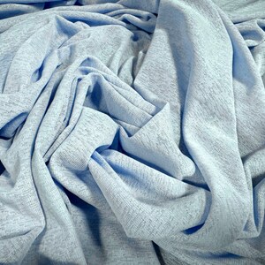 May include: A close-up of a light blue fabric with a textured surface. The fabric is wrinkled and folded, creating a soft and drapey look.