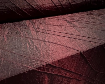May include: Close-up of a deep burgundy fabric with a crinkled texture. The fabric has a subtle sheen and is folded in a way that creates diagonal lines.