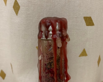 May include: A glass bottle with a red wax seal and a clear glass body filled with a mixture of herbs and crystals. The wax is dripping down the sides of the bottle.