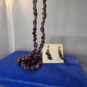 May include: A vintage jewelry set featuring a long necklace and matching earrings. The necklace and earrings are made of dark brown, oval-shaped beads with red accents. The earrings are on a small card that says "Handmade in Hawaii."
