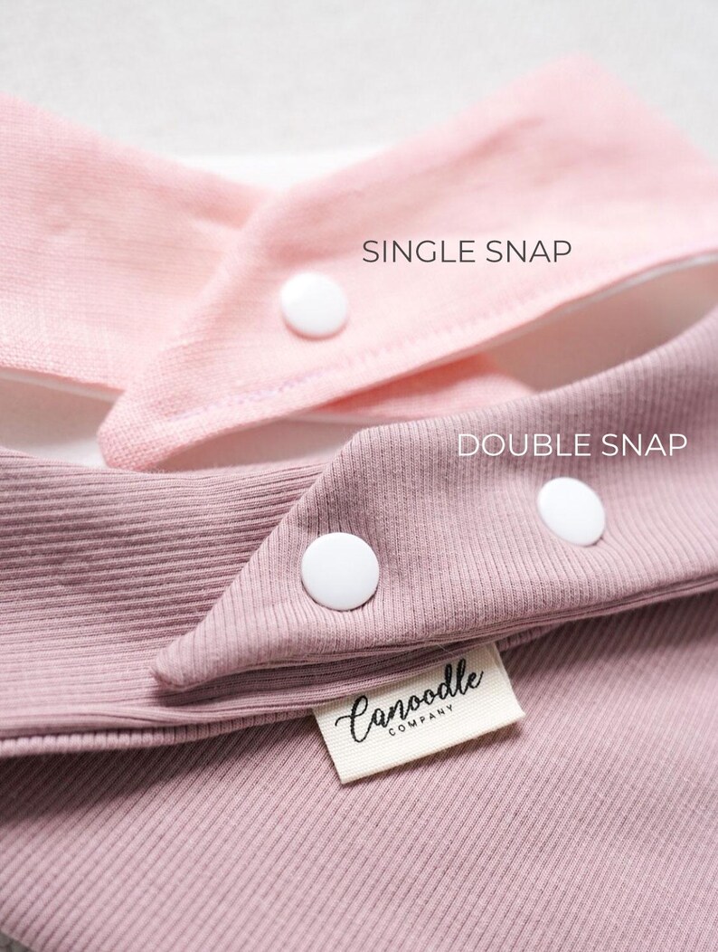 May include: Two ribbed fabric bibs in light pink and dusty rose. The light pink bib features a single white snap, labeled SINGLE SNAP. The dusty rose bib features two white snaps, labeled DOUBLE SNAP, and a white tag reading Canoodle COMPANY.