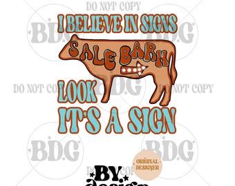 May include: A brown cow illustration with the words "I BELIEVE IN SIGNS" and "SALE BARN" in a retro font. The text "LOOK IT'S A SIGN" is also included. The design includes the text "BY design Graphics".