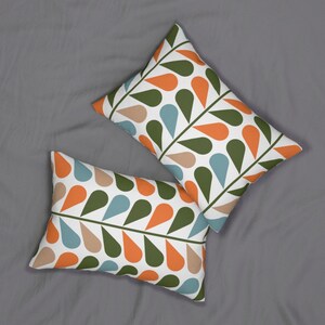 Op de afbeelding: Twee rechthoekige kussens met een witte achtergrond en een herhalend patroon van druppelvormen in oranje, groen, bruin en blauw. De druppels zijn gerangschikt langs een donkergroene, stengelachtige lijn.